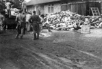 Camp de concentration de Dachau – les prisonniers enlèvent de la plate-forme les corps des morts ; au second plan – bâtiment du crématorium [1945]. (AIPN)